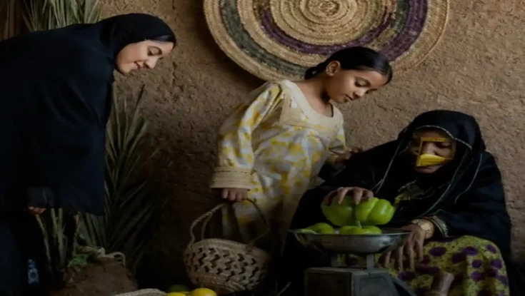Women and a young girl weighing fresh produce in a traditional rural marketplace setting.